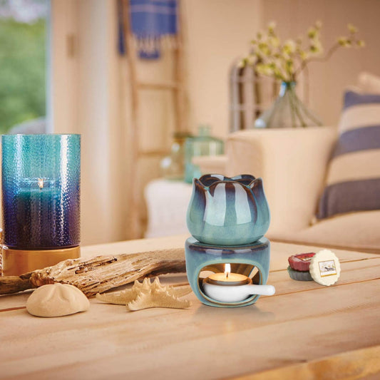 VibraMist Eternal Bloom fragrance warmer with a glowing tealight, styled on a wooden table beside shells, driftwood, and a blue glass candle.