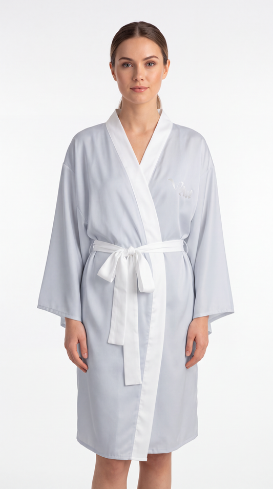 A woman modeling a light blue bathrobe with a white collar, front trim, belt, and tie, photographed against a plain white studio background.