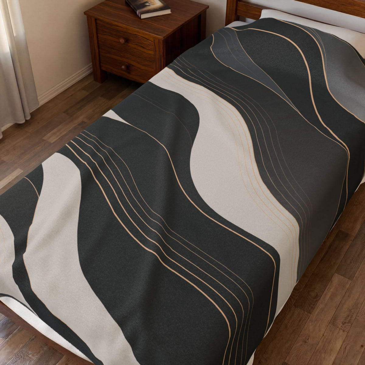A bed in a bedroom setting featuring a dark gray and off-white wavy abstract patterned blanket with thin gold accent lines.